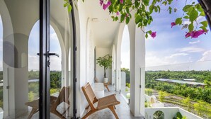 A balcony with a view of a lush landscape, white columns, and wicker furniture. - Unu Villa by Betterplace (Canggu)