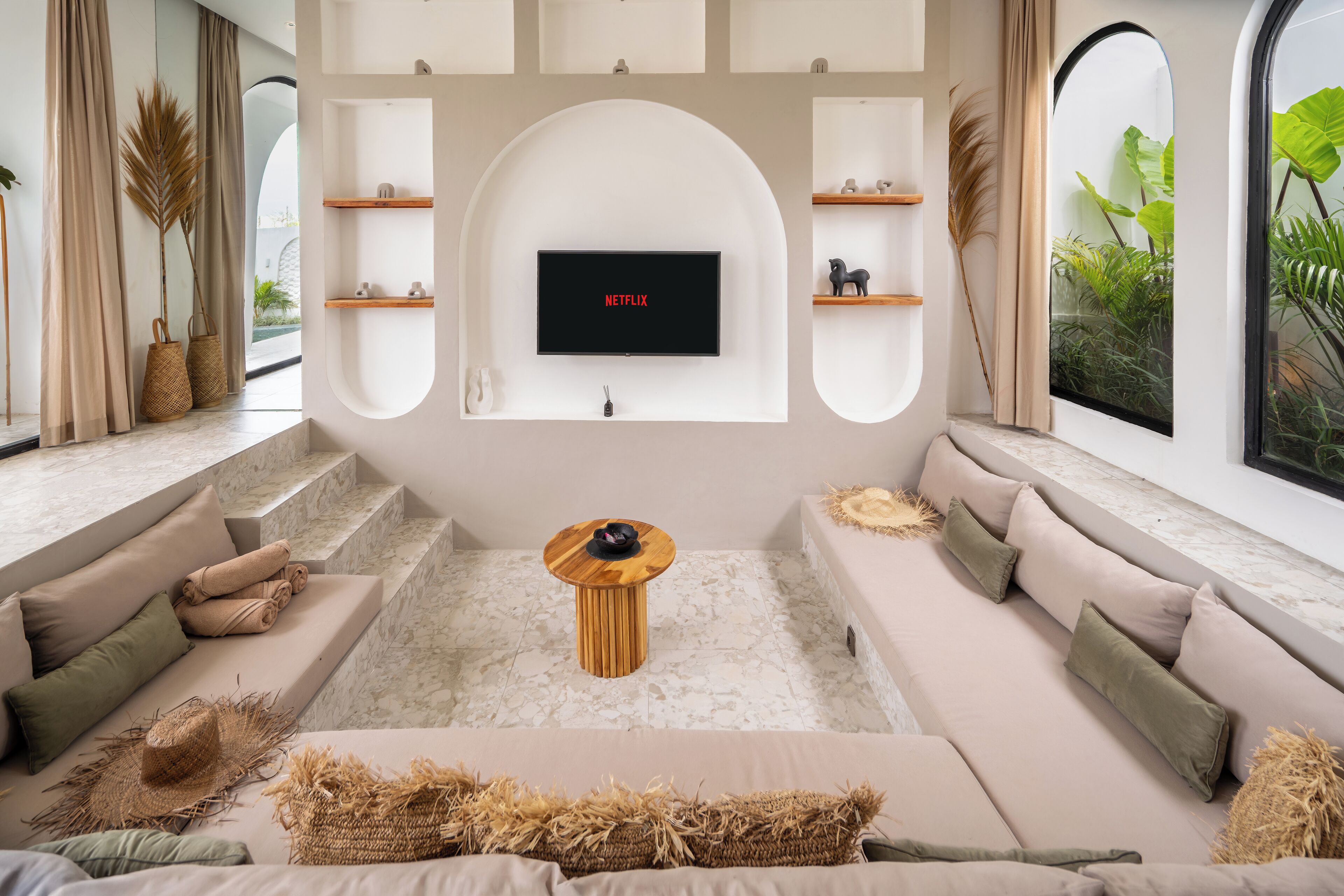 Una sala de estar moderna con un televisor de pantalla plana montado en una pared blanca, una mesa de centro de madera y un sofá color beige con cojines.