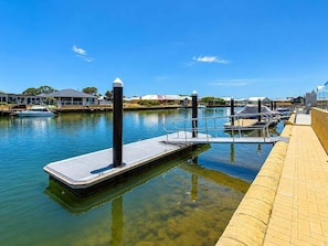 A marina with docked boats, a clear blue sky, and a paved walkway along the water.
