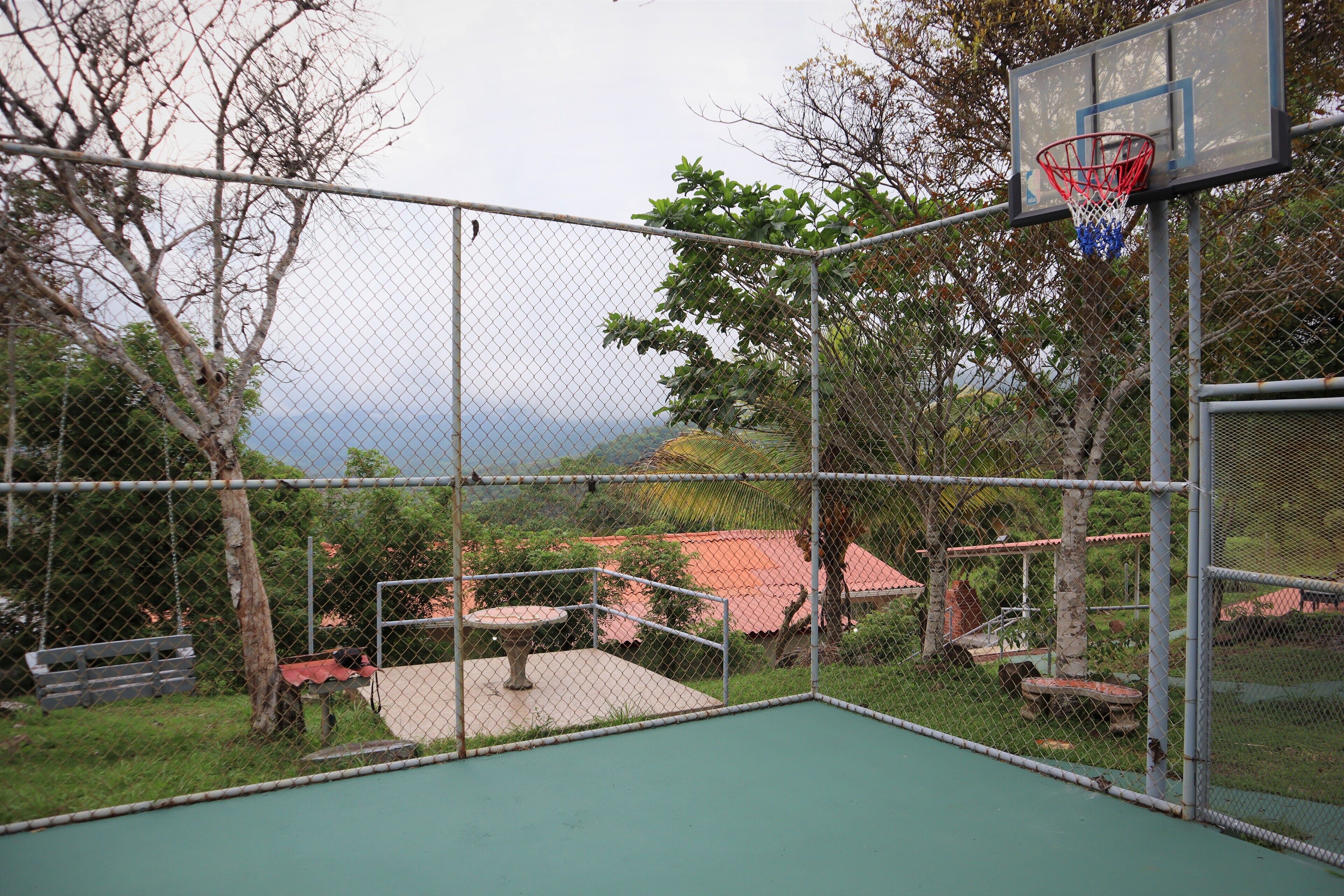 Een basketbalveld buiten, met een hek van gaas, een basketbalring en een bank.