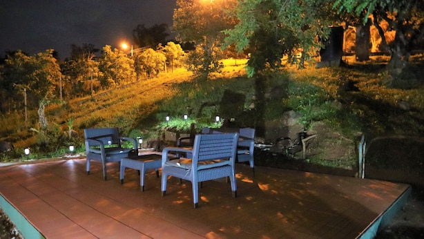 An outdoor seating area with chairs and tables, surrounded by greenery and a stone wall.