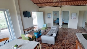 A spacious room with a long sofa, a dining table, and a kitchen area.
