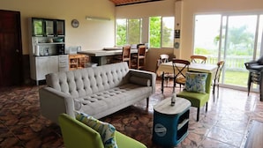 A living area with a sofa, chairs, a coffee table, a kitchen area with cabinets and a microwave, and a dining area with a table and chairs.
