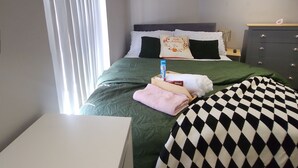 Ein Schlafzimmer mit einem Bett, einem Schminktisch, einem Nachttisch und einem Fenster mit Jalousien.