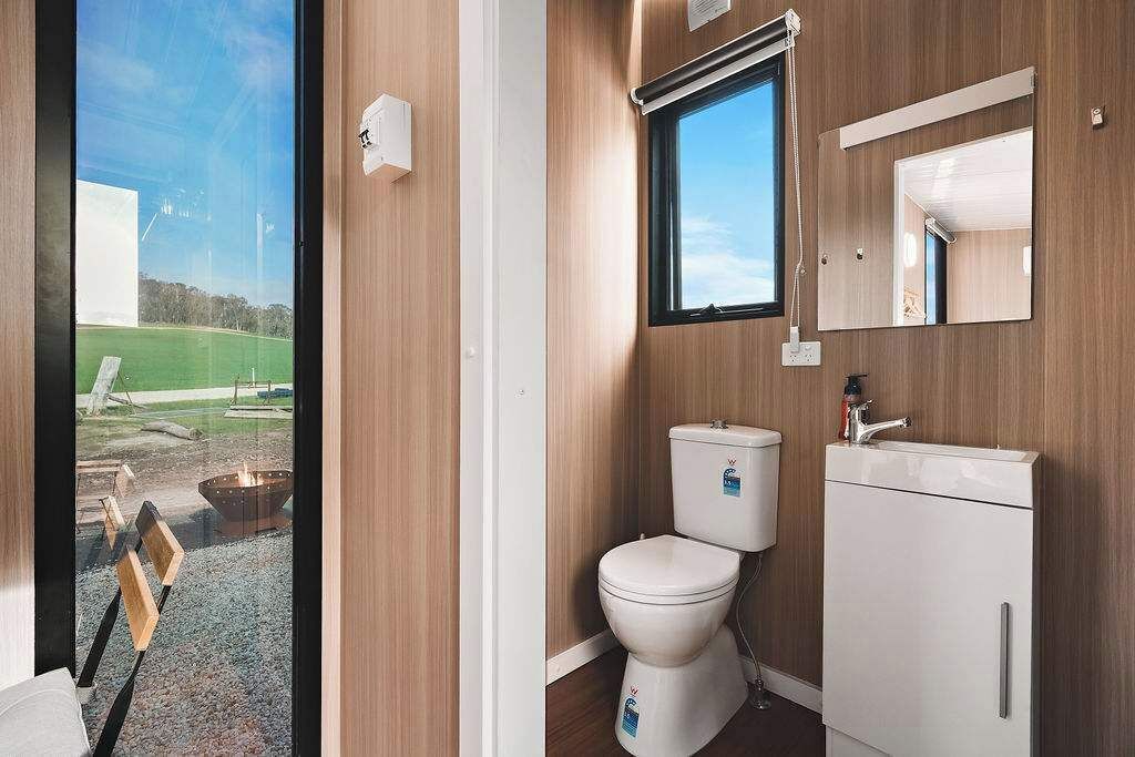 Un baño con inodoro, lavamanos y espejo, paredes de madera y una ventana.
