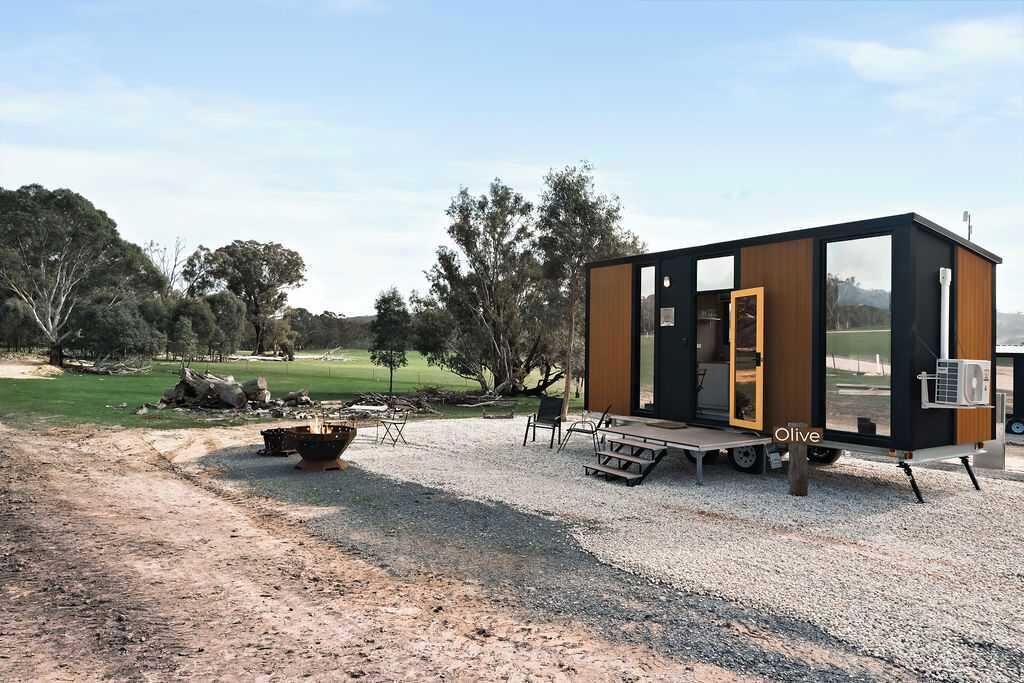 Eine moderne, kompakte Holzhütte mit einer großen Schiebetür, einer kleinen Terrasse und einem Kiesgrundstück.