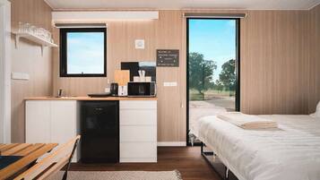 Une chambre d’hôtel moderne équipée d’une kitchenette, d’un lit et d’une grande fenêtre donnant sur l’extérieur.