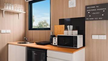 A compact kitchen with a wooden countertop, a sink, a microwave, and a toaster. A welcome sign and a window are also visible.