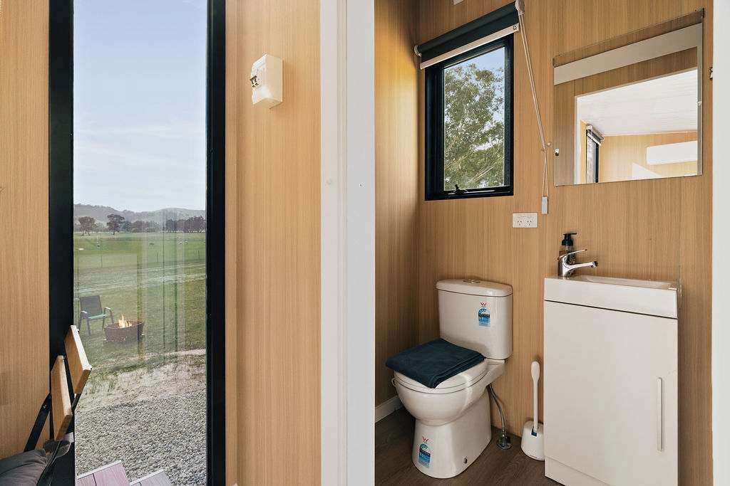 Een kleine badkamer met toilet, wastafel en een raam met uitzicht op een grasveld.