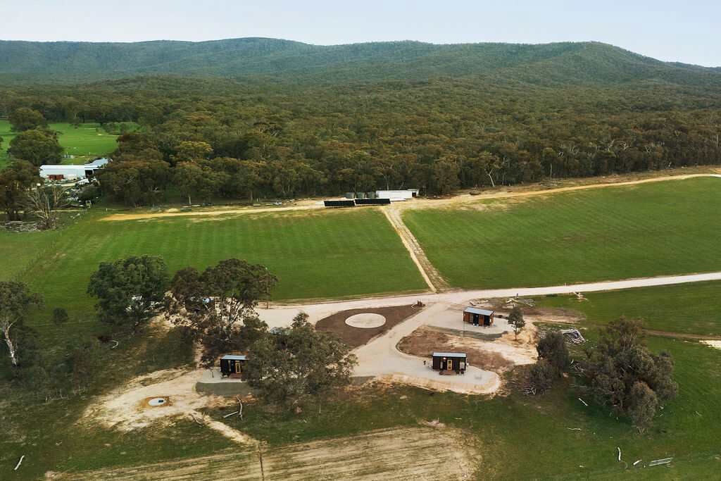 Vista aérea de una propiedad rural con varias construcciones, campos abiertos y un paisaje montañoso.