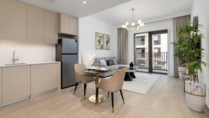 A modern kitchen with beige cabinets, a black refrigerator, and a dining area with two chairs and a round table. - Maison Privee - Charming Urban Escape with Resort-Style Facilities (Dubai)