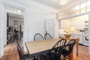 A dining area with a wooden table and chairs, white cabinetry, and a kitchen in the background. - Prime Location, Recently Redesigned, Riverfront! (Great Barrington)