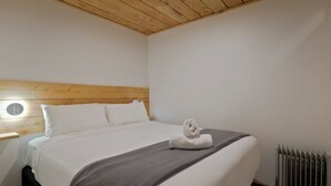 A hotel room with a wooden headboard, a bed with white linens, a grey bedspread, and a rolled towel on the bed. - Central Lofts Unit 4 (Queenstown)