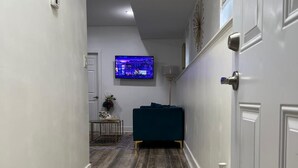 A hallway with wooden flooring, a television mounted on the wall, and a blue sofa. - Welcome To The Great Place Of Life (Saskatoon)
