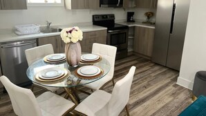 A modern kitchen with a dining area. It includes a glass table with white chairs, a vase with flowers, and stainless steel appliances. - Welcome To The Great Place Of Life (Saskatoon)