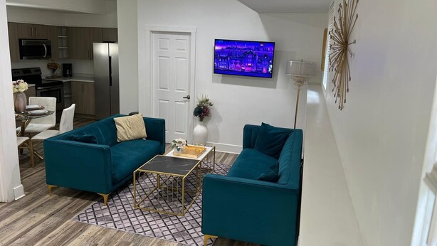 A modern living room with teal sofas, a coffee table, and a TV mounted on the wall. - Welcome To The Great Place Of Life (Saskatoon)