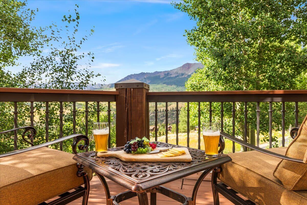 Ein Balkon mit zwei gepolsterten Stühlen, einem Holztisch und zwei Biergläsern.