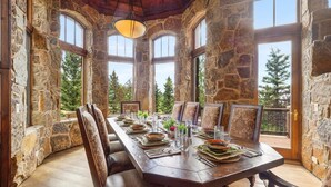 A stone-walled dining room with a wooden table set for six, large windows, and a view of trees. - Luxe Mountain Village Retreat | Hot Tub + Shuttle (Mountain Village)