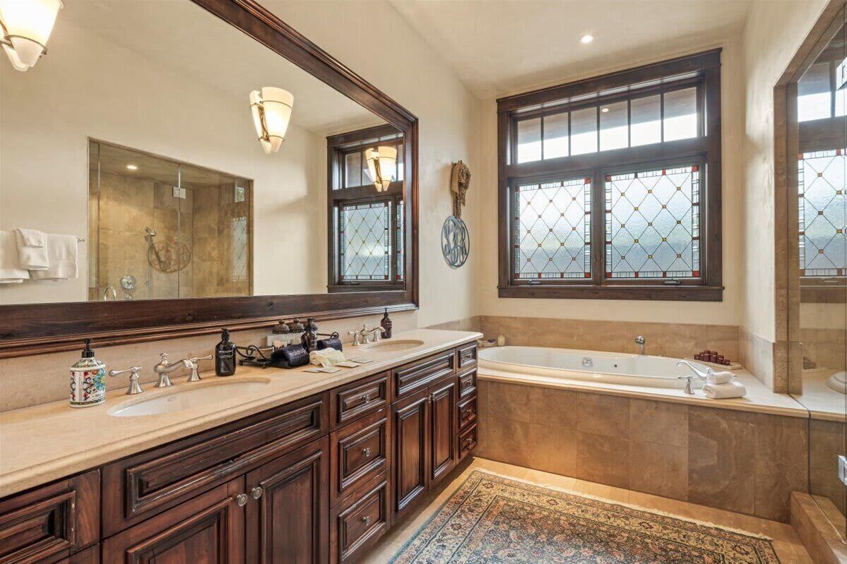 A spacious bathroom with a large mirror, two sinks, a bathtub, and a window with a view.