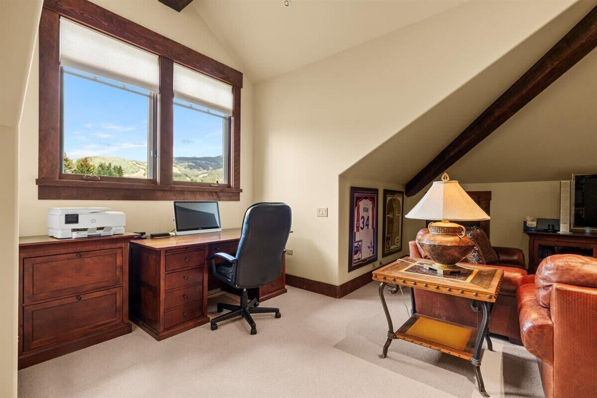 A room with a desk, computer, office chair, lamp, and a view of the outdoors.