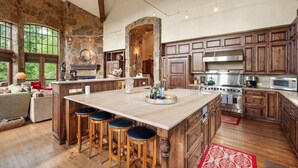 A spacious kitchen with a large island, wooden cabinets, and a stone accent wall. - Luxe Mountain Village Retreat | Hot Tub + Shuttle (Mountain Village)