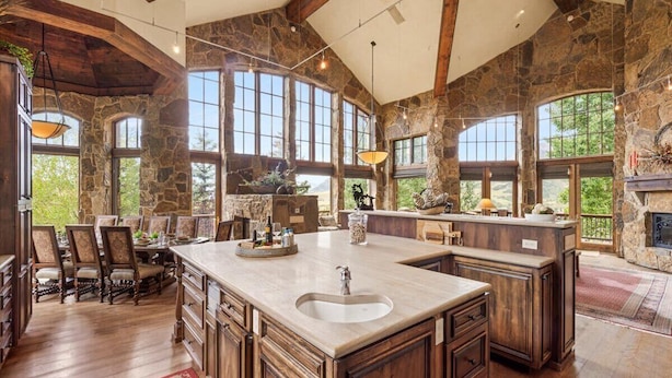 A spacious kitchen with a large island, stone walls, and large windows offering views of the outdoors. - Luxe Mountain Village Retreat | Hot Tub + Shuttle (Mountain Village)