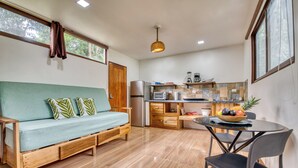 Een knus woongedeelte met een bank, een eettafel met stoelen, een keuken met inbouwapparatuur en een raam voor natuurlijk licht.