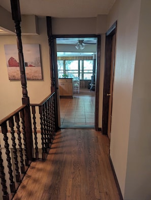 A wooden staircase leading to a kitchen with a large window, a ceiling fan, and a door to another room.