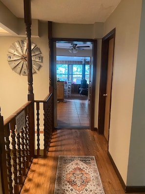 A wooden staircase with a clock, a rug, and a view into a living room with a fireplace.