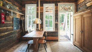 A rustic wooden interior with a wooden table, chairs, and a lamp. There are two windows with shutters and a door leading outside. - Stay North - Honkala (Turku)
