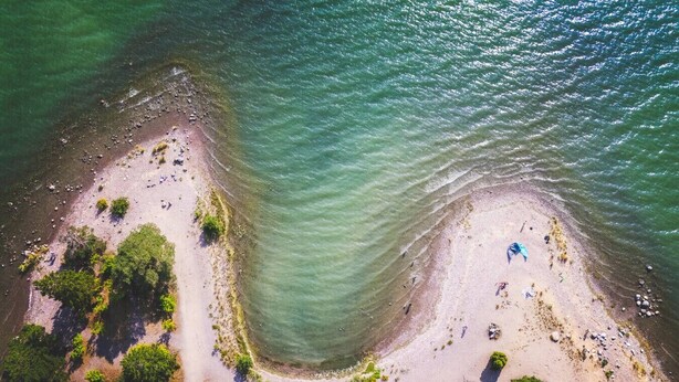 An aerial view of a beach with clear water, sandy shore, and dense greenery. - Stay North - Honkala (Turku)