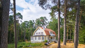 A two-story house with a red roof, surrounded by tall trees and a dirt path leading to it. - Stay North - Honkala (Turku)
