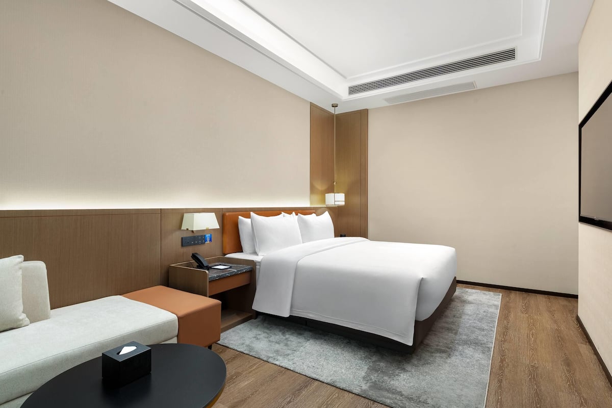 Una habitación de hotel con cama, sofá, mesita de noche, lámpara y televisor.