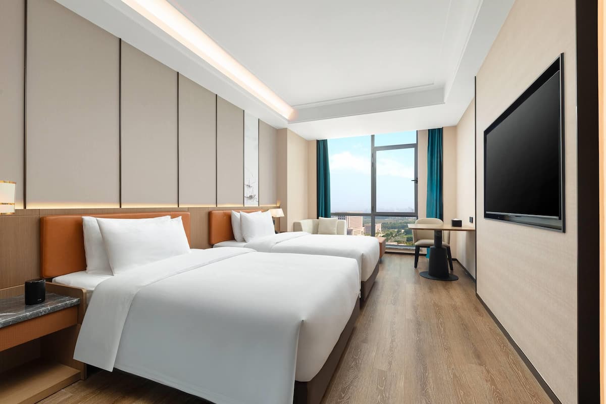 Habitación de hotel con dos camas, un escritorio, un televisor y vista a la ciudad.