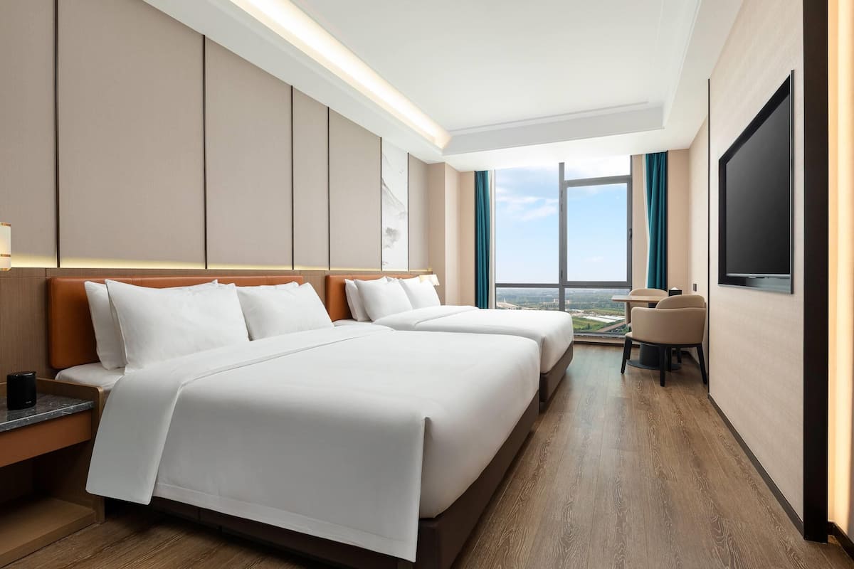 Habitación de hotel con dos camas, televisión, escritorio y vista a la ciudad.
