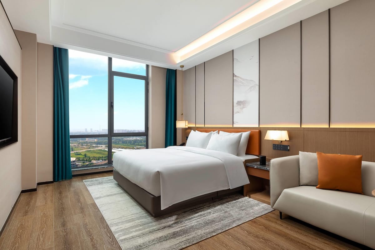 Una habitación de hotel moderna con una cama grande, un sofá, un escritorio y vistas a la ciudad.