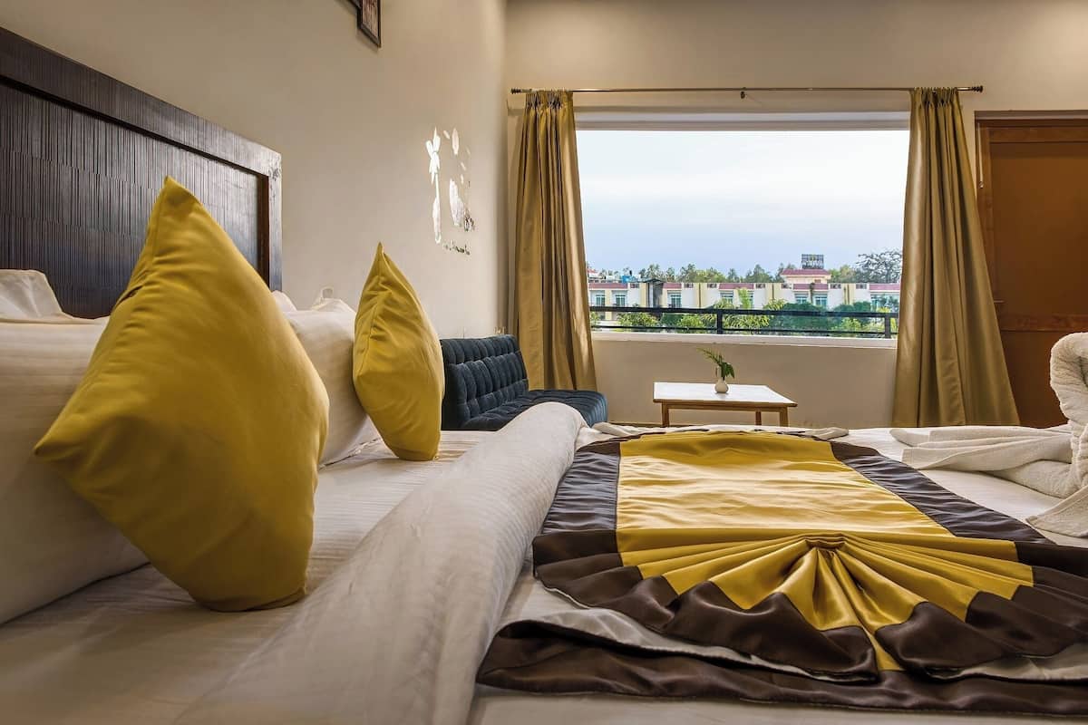 A hotel room with two beds, a view of buildings through the window, and a small table with a plant.