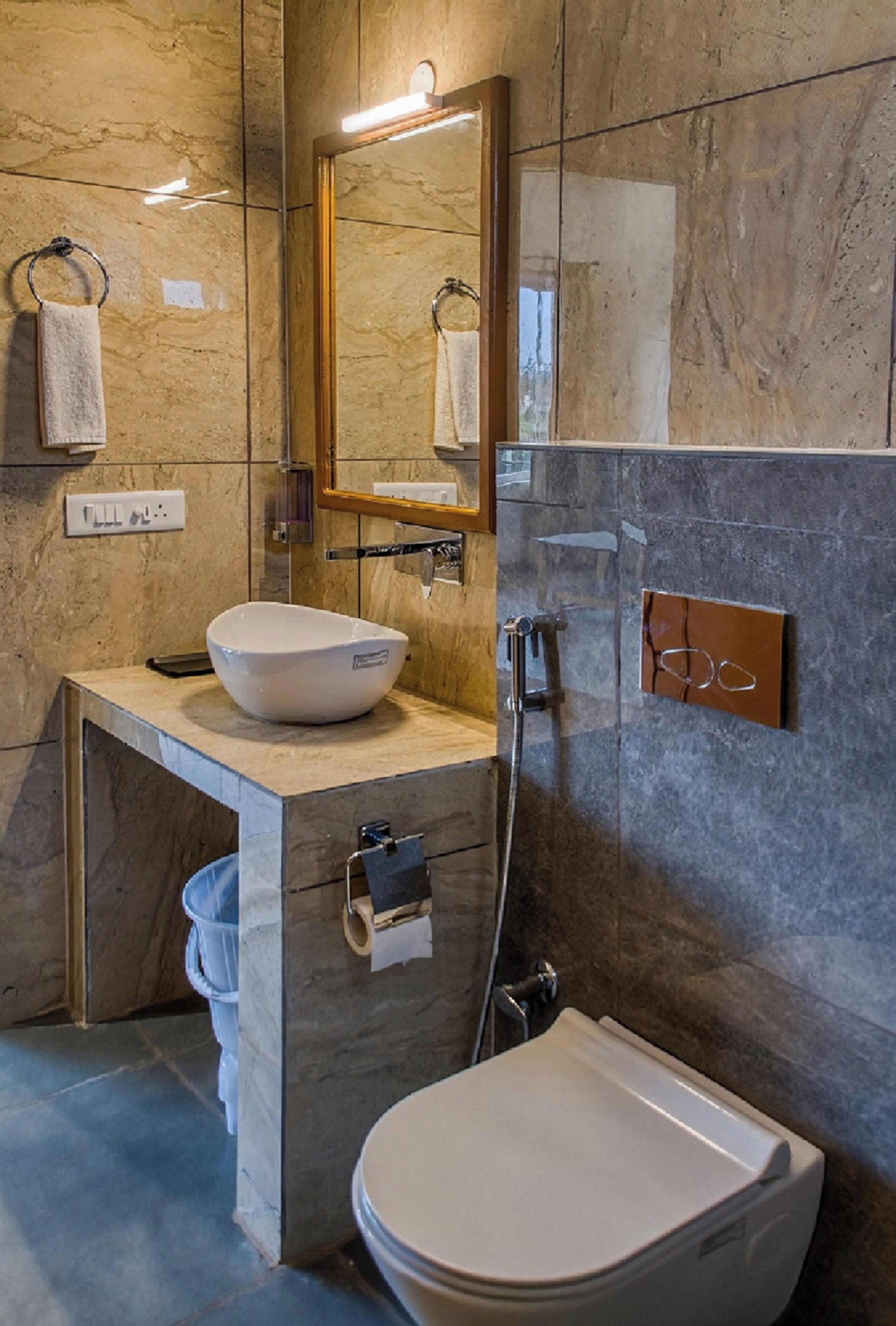 A modern bathroom with a marble wall, a large mirror, a vessel sink, a toilet, and a shower.