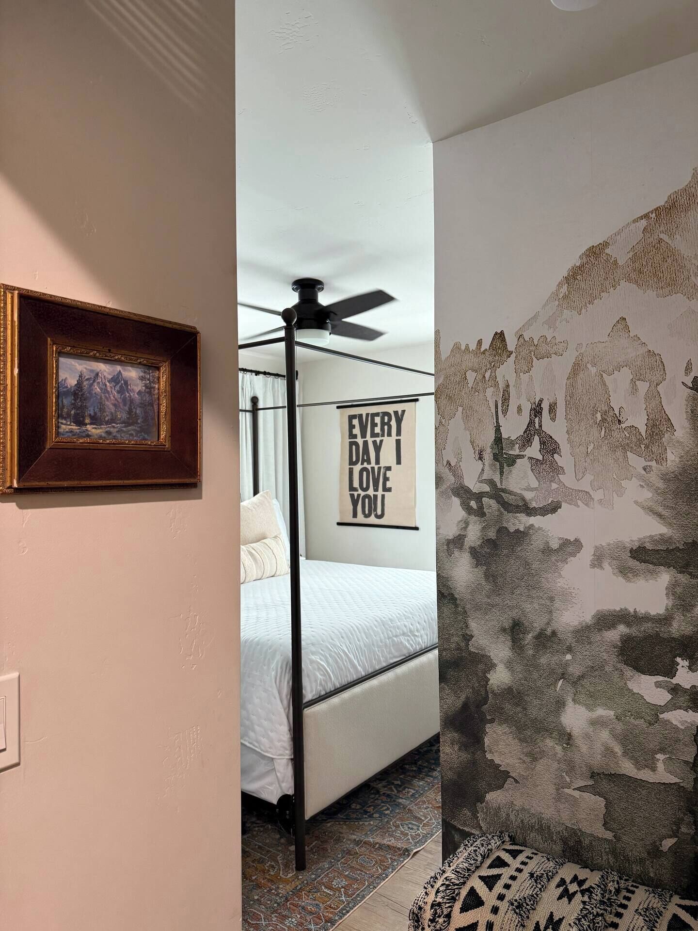 Un dormitorio con cama, ventilador de techo, un cuadro enmarco y un cartel motivacional.