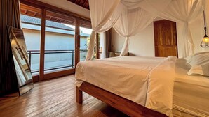 Un dormitorio con cama de madera, ropa de cama blanca y dosel. Hay una puerta corrediza de vidrio que da a un balcón.