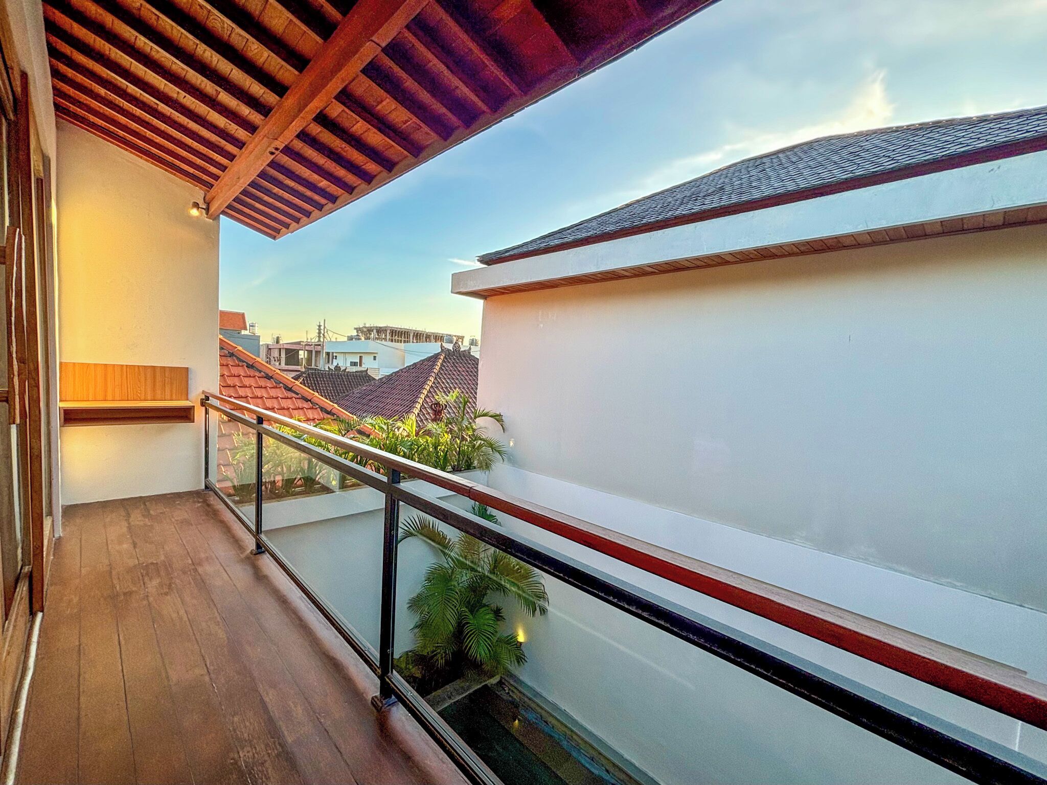 A balcony with a wooden floor and a glass railing overlooking a cityscape.