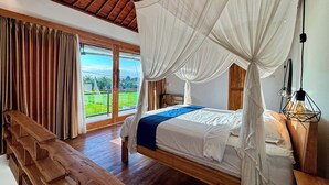Un dormitorio con cama con dosel, suelo de madera, un banco y vistas a un paisaje verde a través de amplios ventanales.