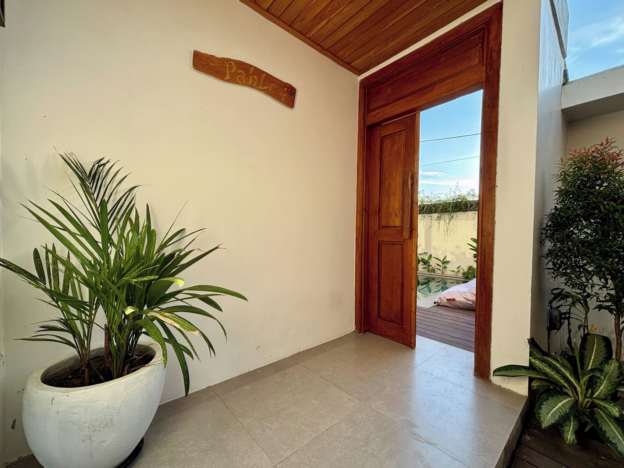 Un pasillo con una planta en maceta, una puerta de madera y un letrero que dice 'Pablo 99'.