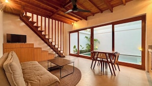 Amplia sala de estar con escalera de madera, un sofá, una mesa de centro y una mesa de comedor con sillas.