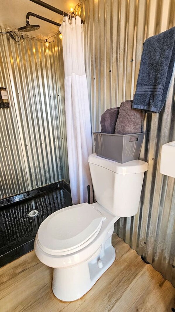 A compact bathroom with a white toilet, a shower area with a curtain, and a towel hanging on the wall.