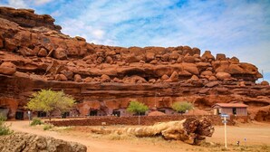 A desert landscape with red rock formations, a small building with a corrugated metal roof, and sparse vegetation. - Cozy Cabin @ Private Moab Ranch (Moab)