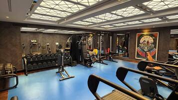 Ein Fitnessraum mit Trainingsgeräten, blauem Boden und einer Dachfenster-Decke.
