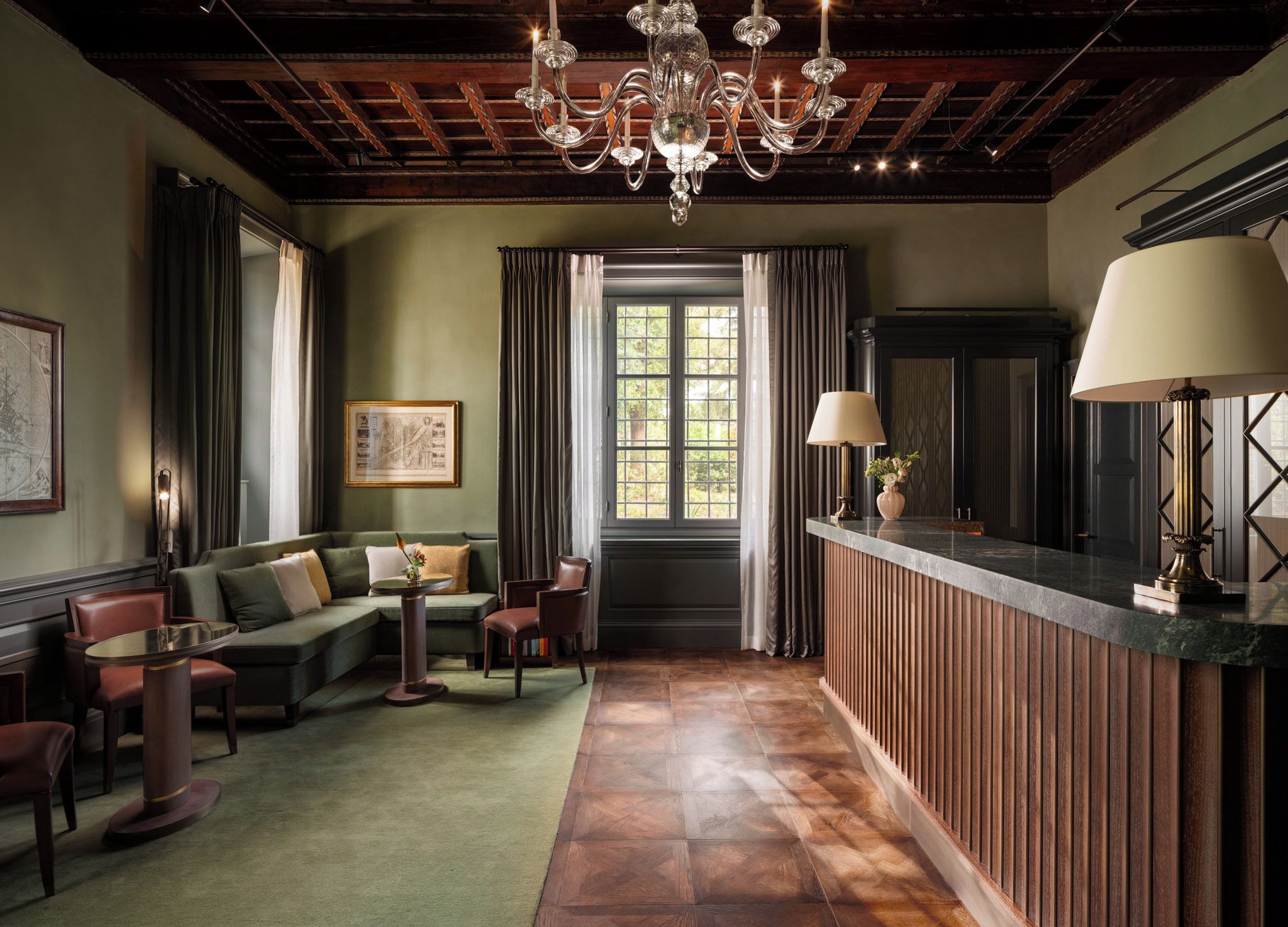 A room with a green sofa, a round table, a chandelier, and a wooden reception desk.