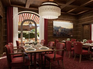 A dining area with wooden tables, red upholstered chairs, and a large painting on the wall.