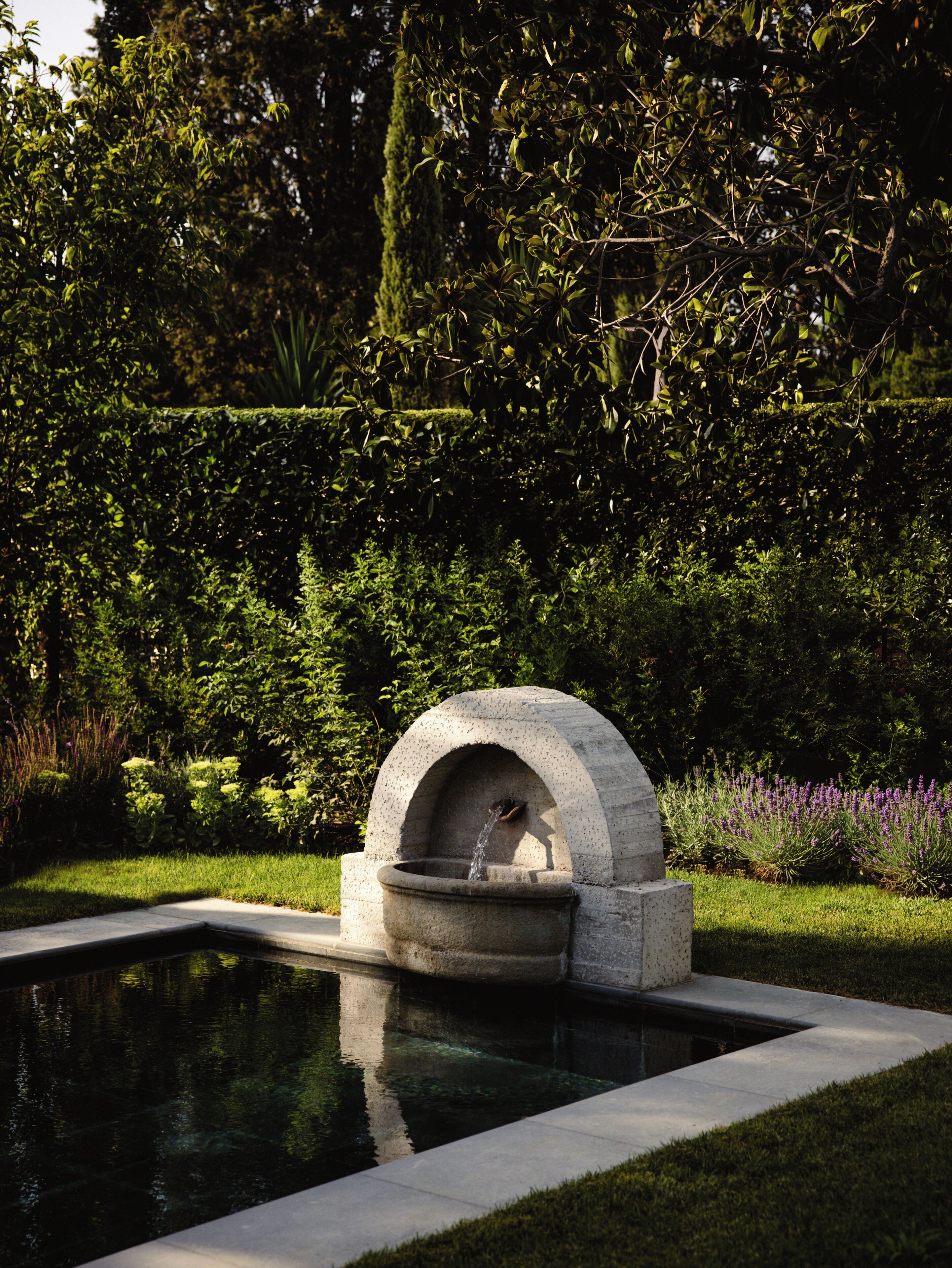 A garden with a water feature, including a stone structure and a rectangular pool.